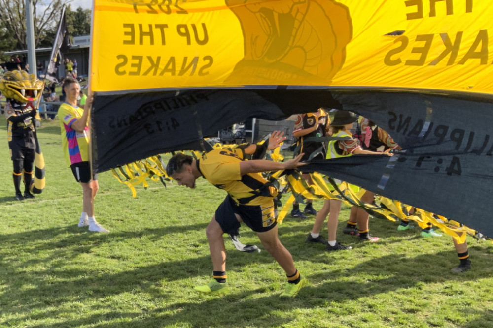 Jayden Alefaio bursts through the banner as he leads the Caboolture Snakes U16 Black Boys team onto the playing arena.