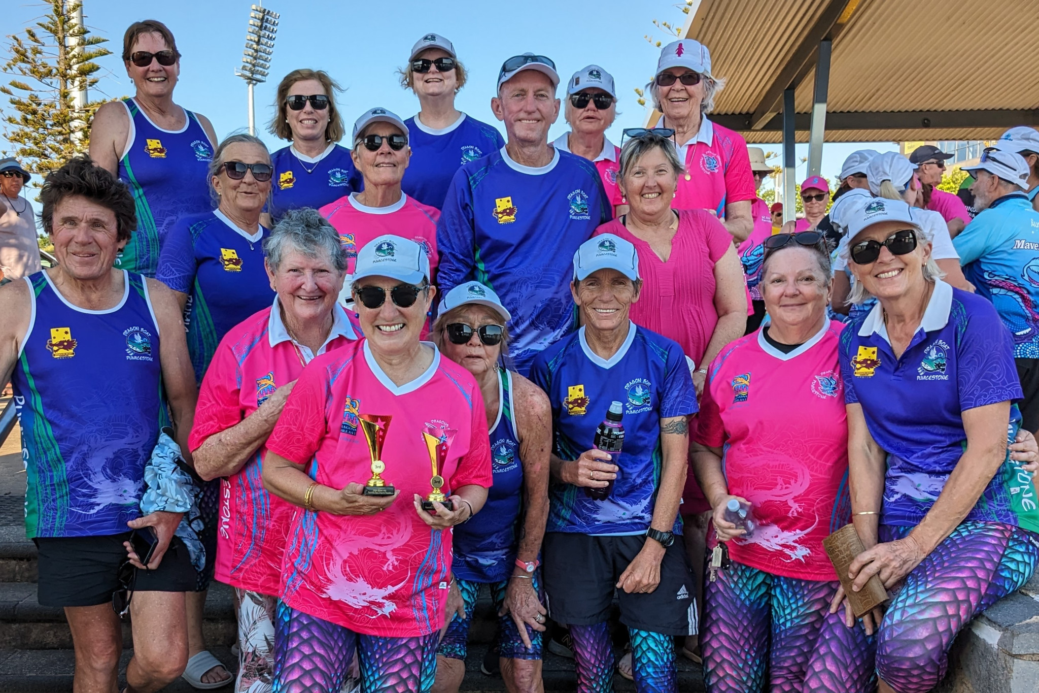 Michelle Hanton proudly shows off trophies, surrounded by Dragon Boat Pumicestone paddlers after the club claimed two third placings at the Redcliffe Red Dragons regatta.