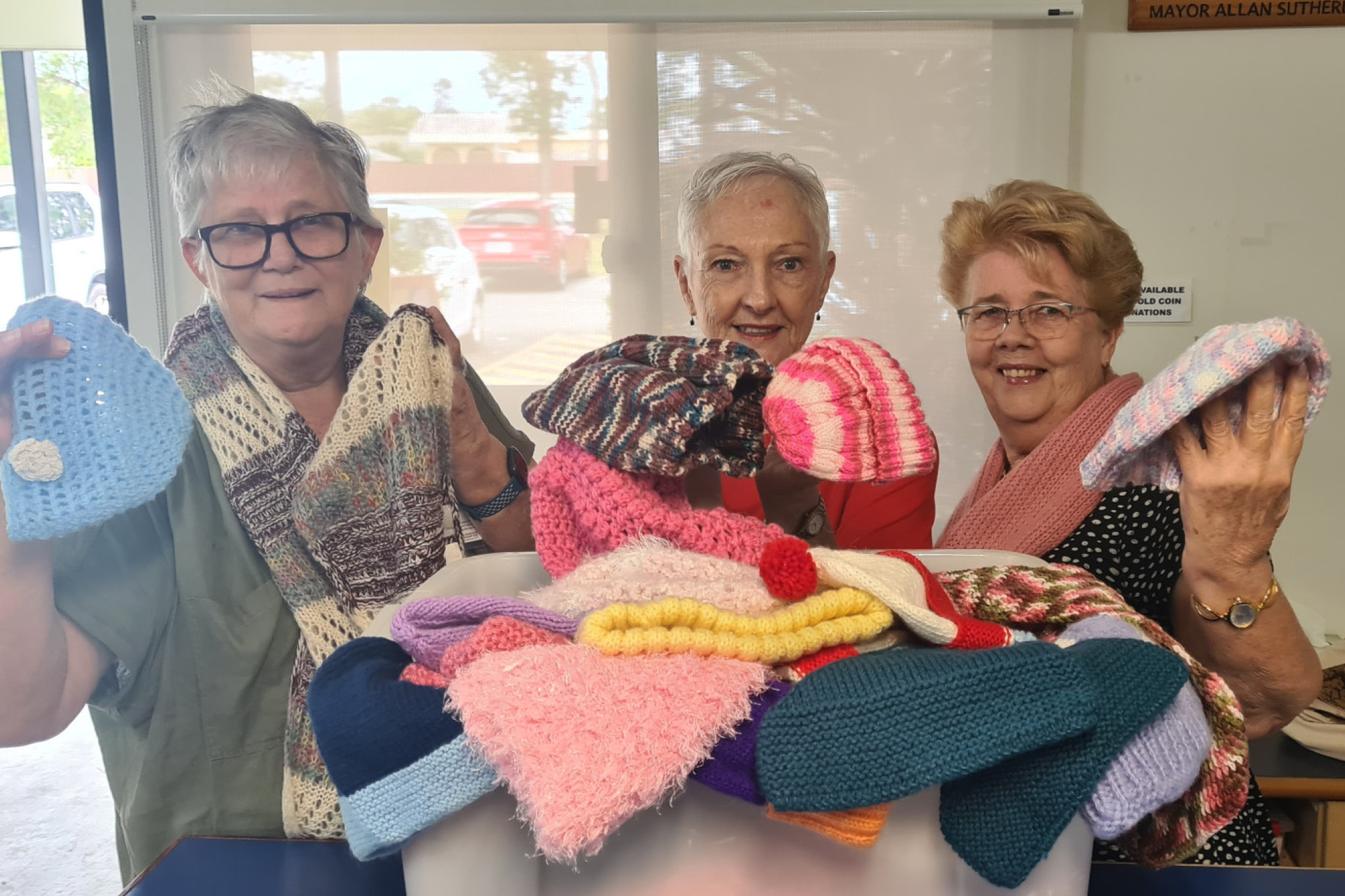 Claire Morgan, Marilyn Boulton and Jan Youngman with knitted hats and scarves donated to Rosies.