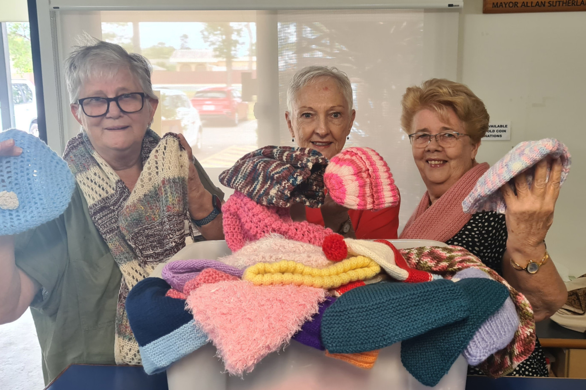 Claire Morgan, Marilyn Boulton and Jan Youngman with knitted hats and scarves donated to Rosies.